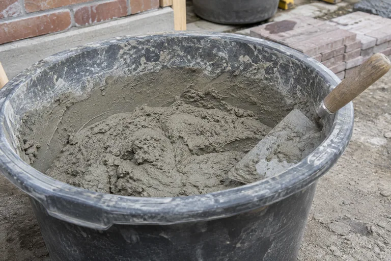 Aangemaakte metselspecie en een troffel in een zwarte kuip.