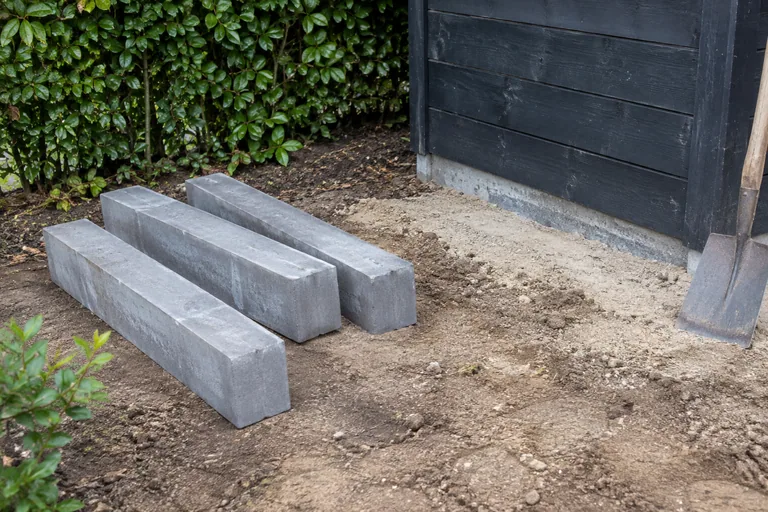 Losse betonnen opsluitbanden naast een houten schuur.
