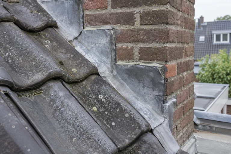 Trapsgewijze loodslabben bij een gemetselde schoorsteen op een pannendak.