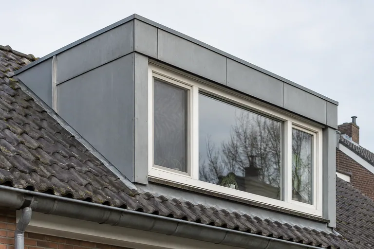 Grijze gevelpanelen rond een witte dakkapel.