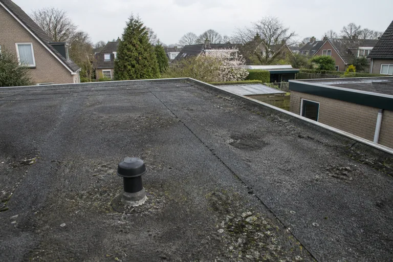 Verweerde zwarte dakbedekking op een plat dak.