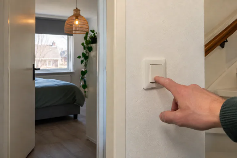 Hand bedient een witte wandschakelaar bij een slaapkamer.