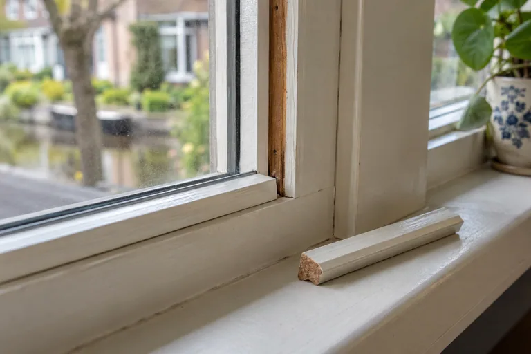 Losse witte glaslat naast een houten raamkozijn.