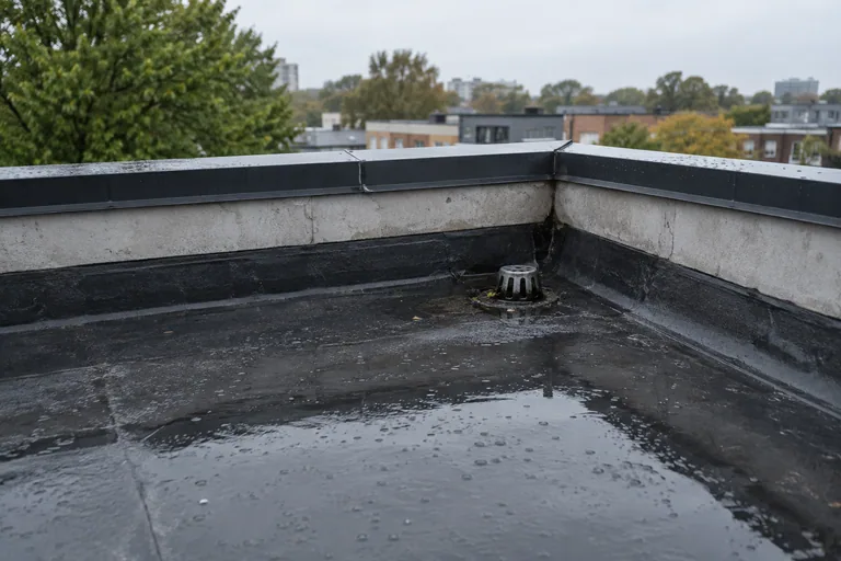 Natte dakbedekking op een plat dak met afvoer in de hoek.