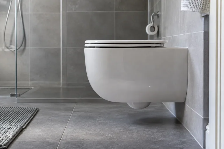 Zijkant van een wandhangend toilet boven een grijze tegelvloer.