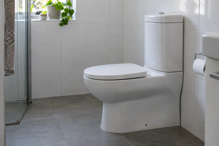 Staand wit toilet met opbouwreservoir op een grijze tegelvloer.