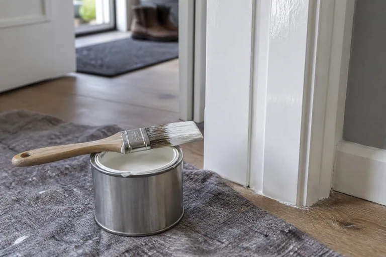Verfblik en kwast naast een wit houten kozijn.