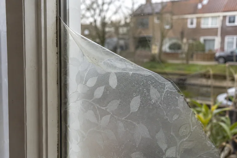 Loskomende raamfolie met patroon op een ruit.