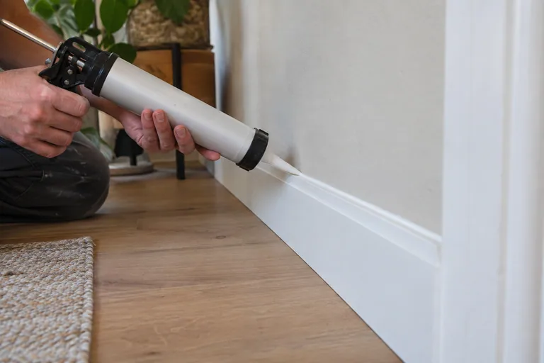 Kitrand aanbrengen tussen een witte plint en een gestucte wand.