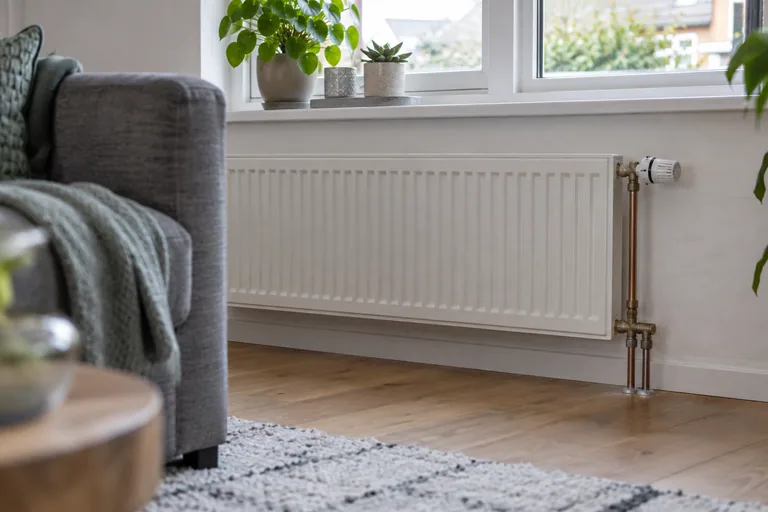 Witte paneelradiator onder een raam naast een bank.