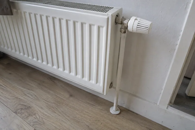 Witte radiatorknop op een metalen kraanhuis met een leiding naar de vloer.