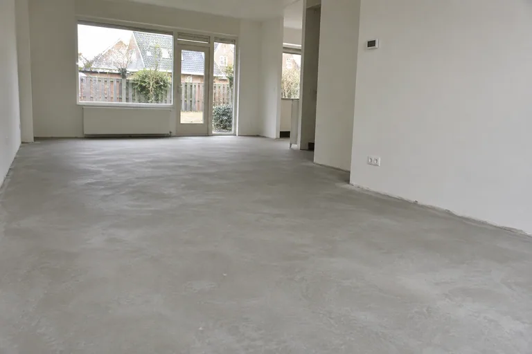 Egale grijze dekvloer in een lege woonkamer tijdens een verbouwing.