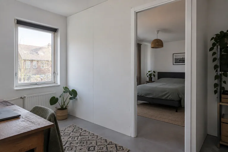 Witte scheidingswand met deuropening tussen twee kamers.