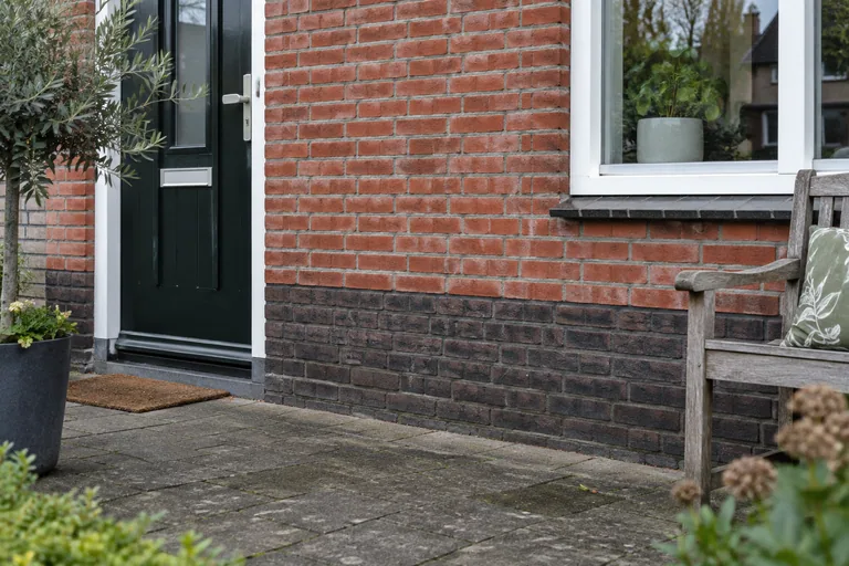 Donkere onderste baksteenlagen aan een gemetselde gevel.