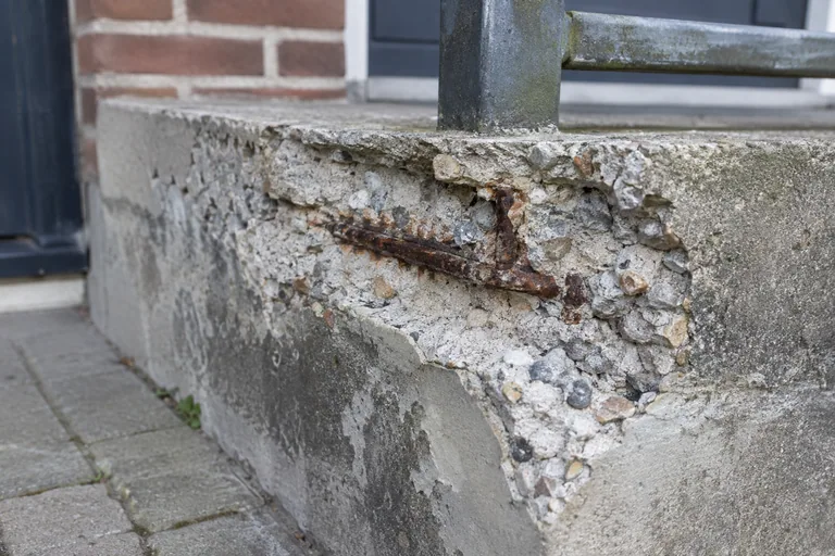 Afgebrokkeld beton met zichtbaar roestig wapeningsstaal.