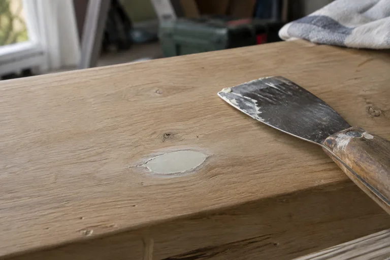 Kleine plamuurplek in een houten plank met een plamuurmes ernaast.