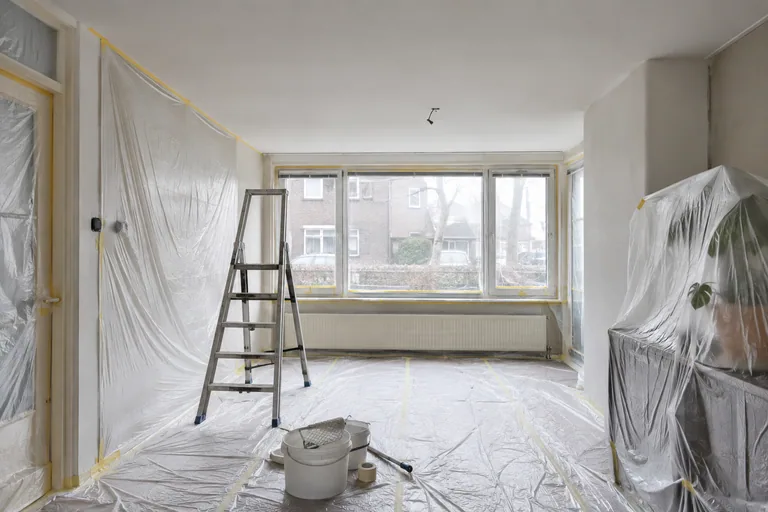 Afgedekte vloer en meubels onder een plafond dat wordt afgewerkt.