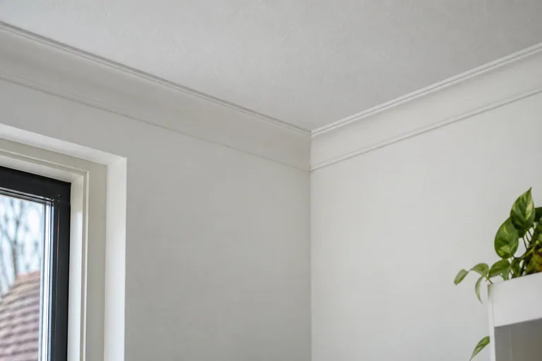 Witte kroonlijst langs de aansluiting van wand en plafond.