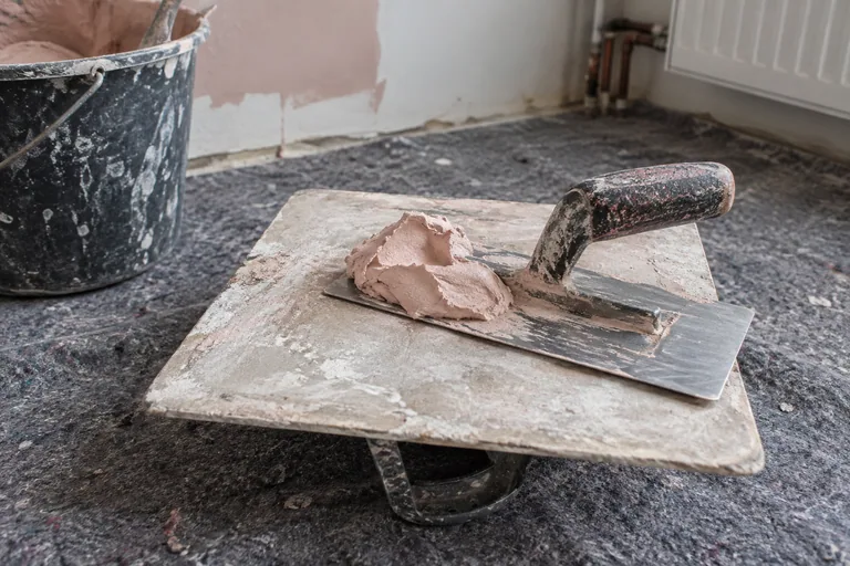 Roze pleister op een raapbord met een metalen pleisterspaan.