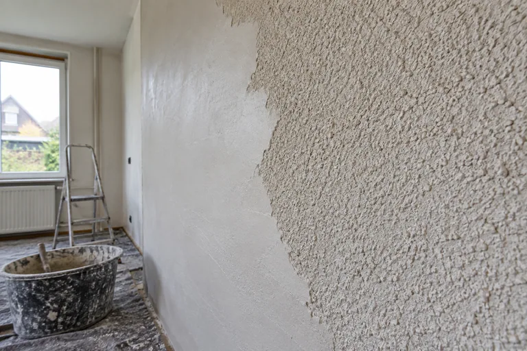 Een grove sierpleisterwand die gedeeltelijk vlak is afgewerkt.