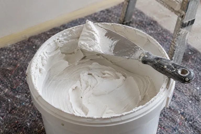 Witte stucpasta in een emmer met een plamuurmes.