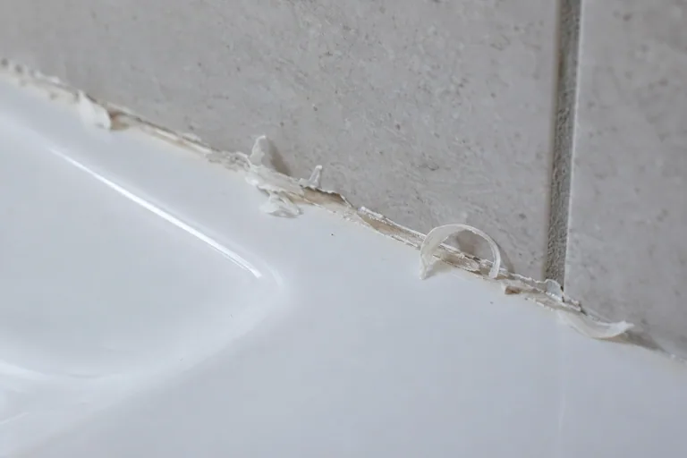 Dunne zichtbare resten van kit op de aansluiting tussen een tegelwand en een witte sanitaire rand.